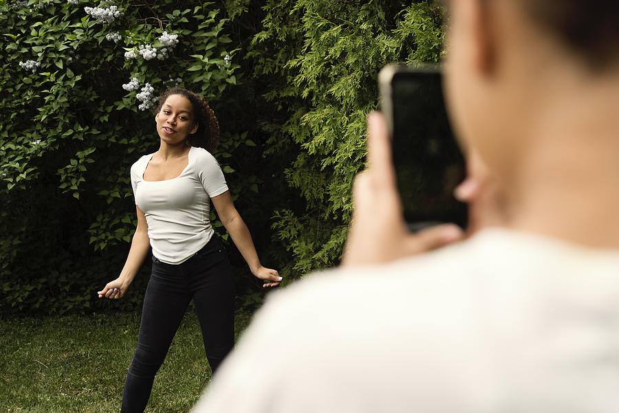 Mixed-race teenage sisters filming with mobile phone in backyard. #1 Photograph by Martinedoucet