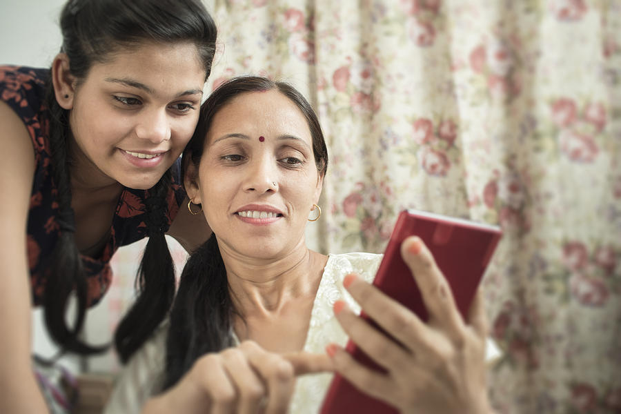 Mother and daughter using phablet together in domestic room. #1 Photograph by Gawrav