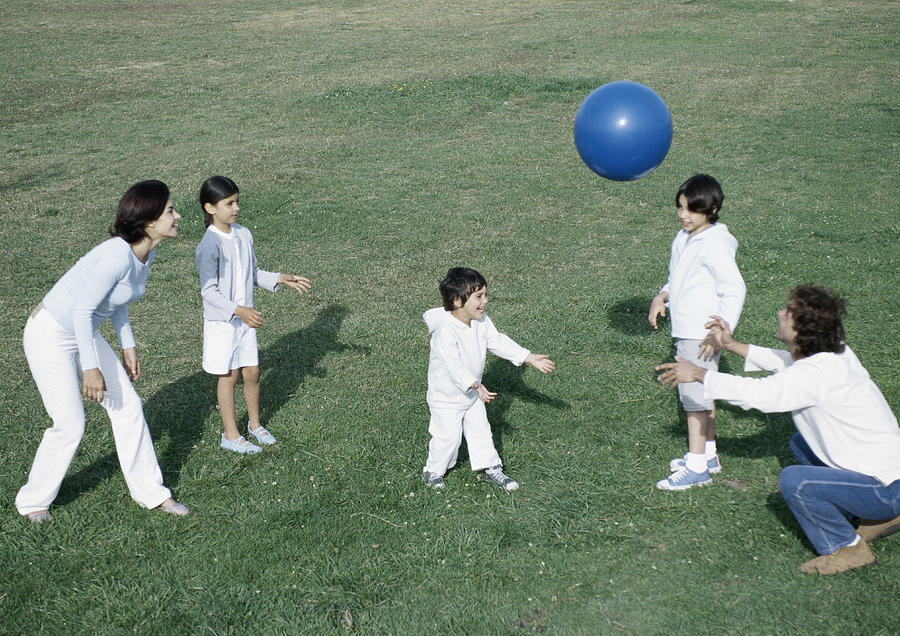 Parents with boys and girl playing ball on grass, full length #1 Photograph by Laurence Mouton
