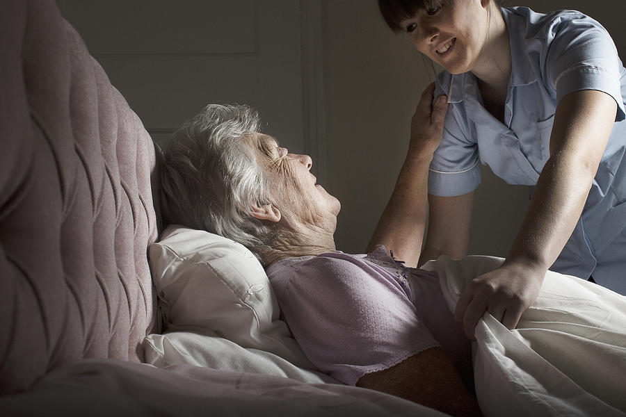 Personal care assistant chatting to senior woman in bed #1 Photograph by Gary John Norman