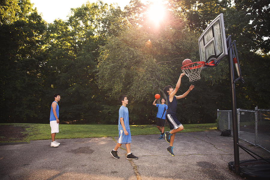 Players playing basketball at court against trees on sunny day #1 Photograph by Cavan Images