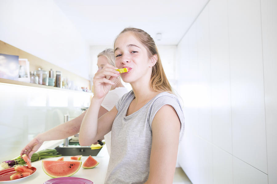 Portrait of smiling teenage girl eating melon in the kitchen #1 Photograph by Westend61