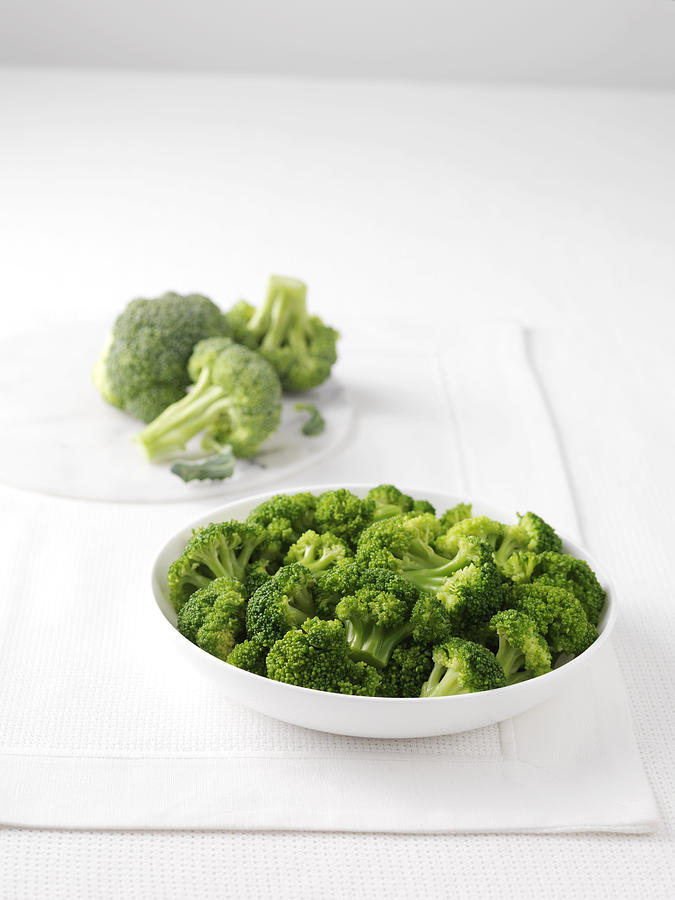 Raw broccoli on marble cutting board and bowl of boiled broccoli #1 Photograph by Diana Miller