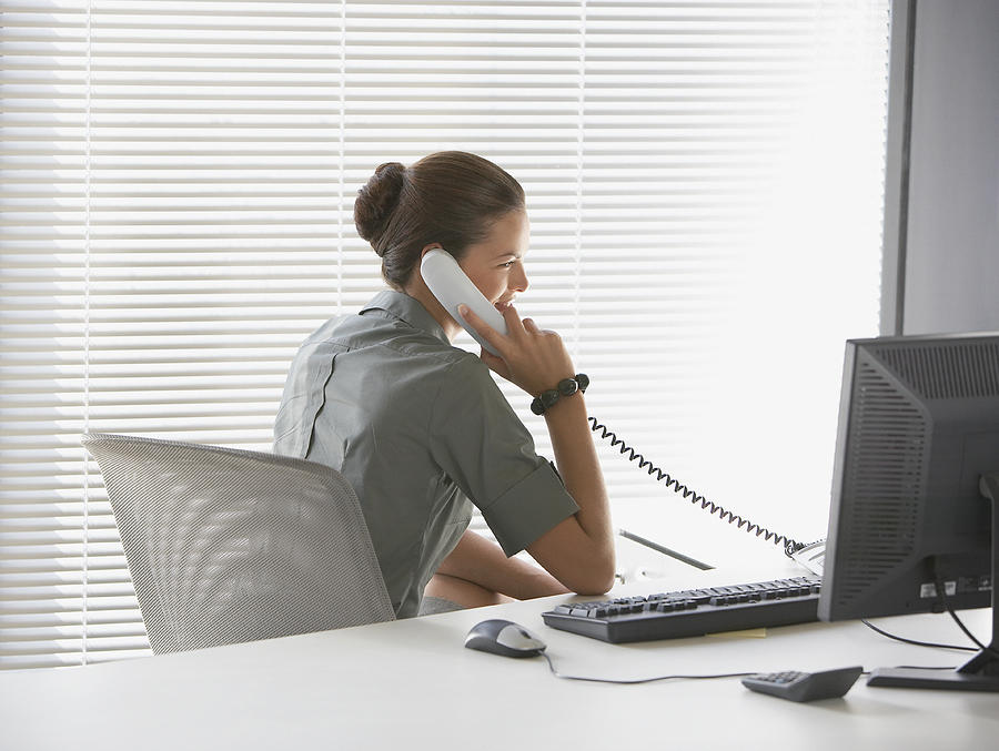 Rear view of businesswoman sitting at desk talking on telephone #1 Photograph by Tom Merton