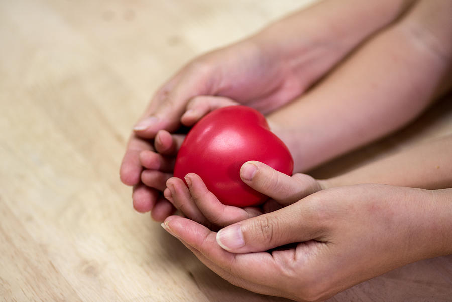 Red heart in child kid and mother hands on wooden table. #1 Photograph by Boonchai Wedmakawand
