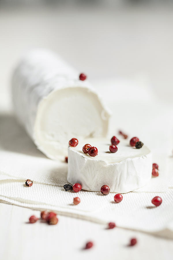 Roll of goats cheese camembert with red peppercorns on white cloth #1 Photograph by Westend61