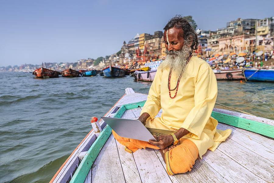 Sadhu using laptop in boat on Holy Ganges River, Varanasi #1 Photograph by Hadynyah
