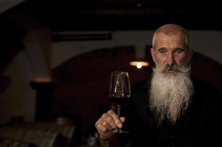 Senior Man with Beard Holding Glass of  Wine in Winecellar #1 Photograph by Neyya