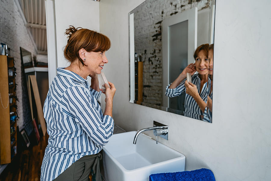 Senior woman adjusting hair in bathroom #1 Photograph by Urbazon
