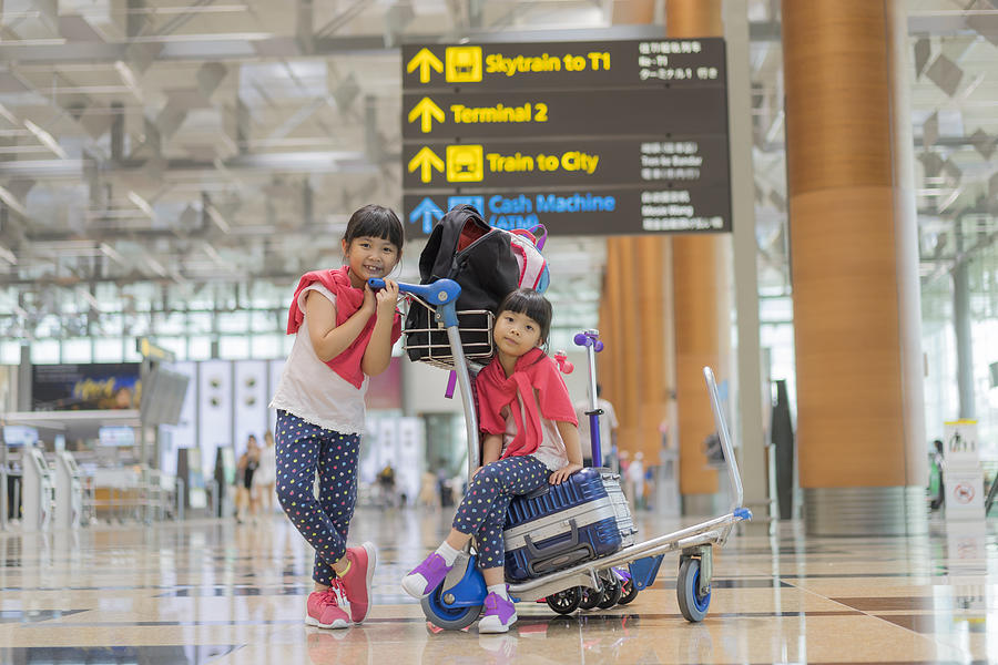 Sisters sitting on suitcases in airport #1 Photograph by Tomatopictures