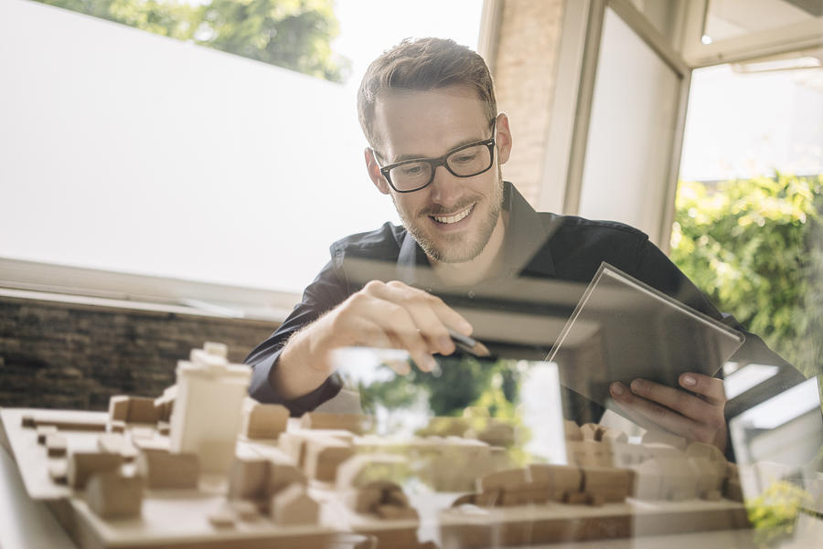 Smiling architect looking at urban development model #1 Photograph by Westend61