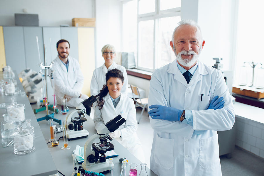 Smiling senior scientist with his colleagues in laboratory #1 Photograph by EmirMemedovski