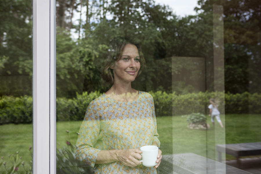 Smiling woman holding cup looking out of window #1 Photograph by Westend61