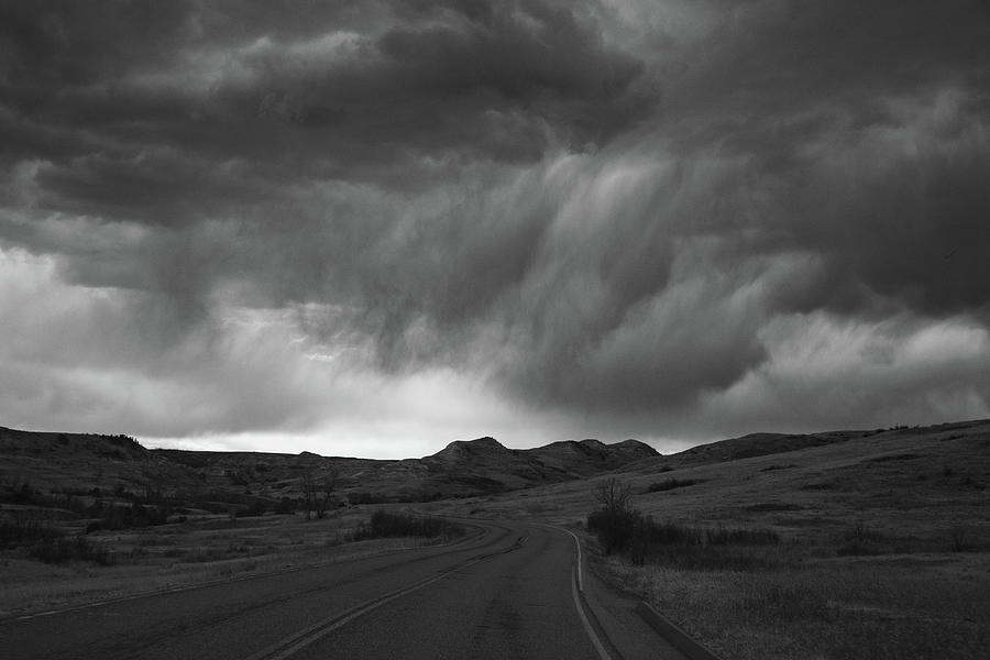 Storm clouds with road at Theodore Roosevelt National Park in North Dakota in black and white #1 Photograph by Eldon McGraw