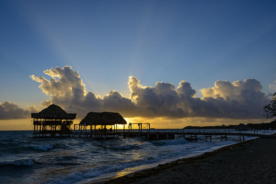 Sunrise at the beach with silhouette of pier with thatched huts #1 Photograph by OGphoto