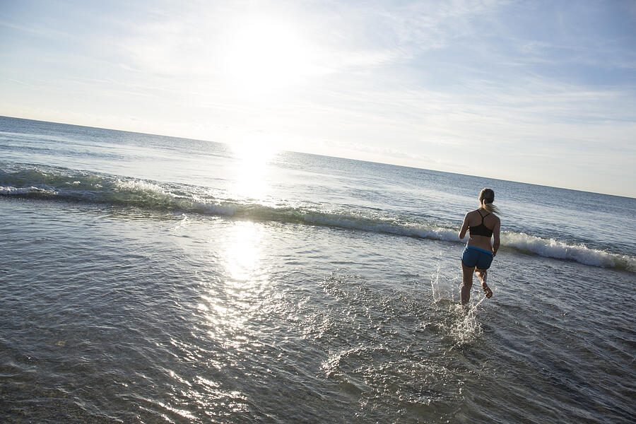 Teen girl runs across beach into waves, gentle surf #1 Photograph by AscentXmedia