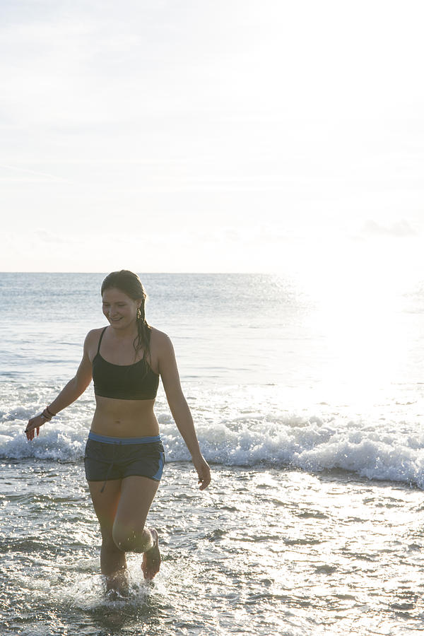 Teen girl walks up beach after swim, gentle surf #1 Photograph by AscentXmedia