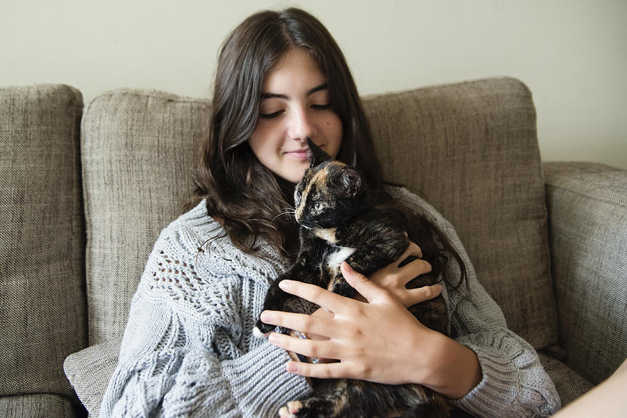 Teenage girl cuddling kitten on living room sofa. #1 Photograph by Martinedoucet