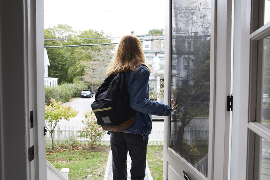Teenage girl walking out the front door of her house. Back view of her leaving the house. She is on her way to school, wearing a back pack and holding the door open. #1 Photograph by Melanie Acevedo