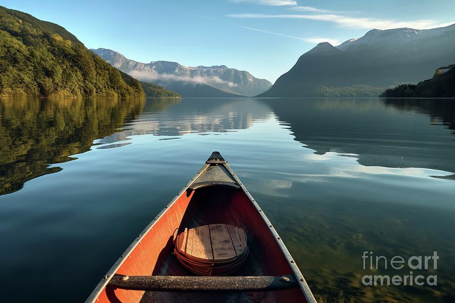 The morning mist cools the calm lake on which a lone canoe float #1 Photograph by Joaquin Corbalan