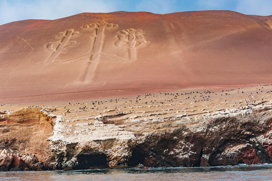 The Paracas Candelabra, also called the Candelabra of the Andes, is a prehistoric geoglyph found on the northern face of the Paracas Peninsula at Pisco Bay in Peru, carved into the red cliffs. #1 Photograph by Oleksandra Korobova