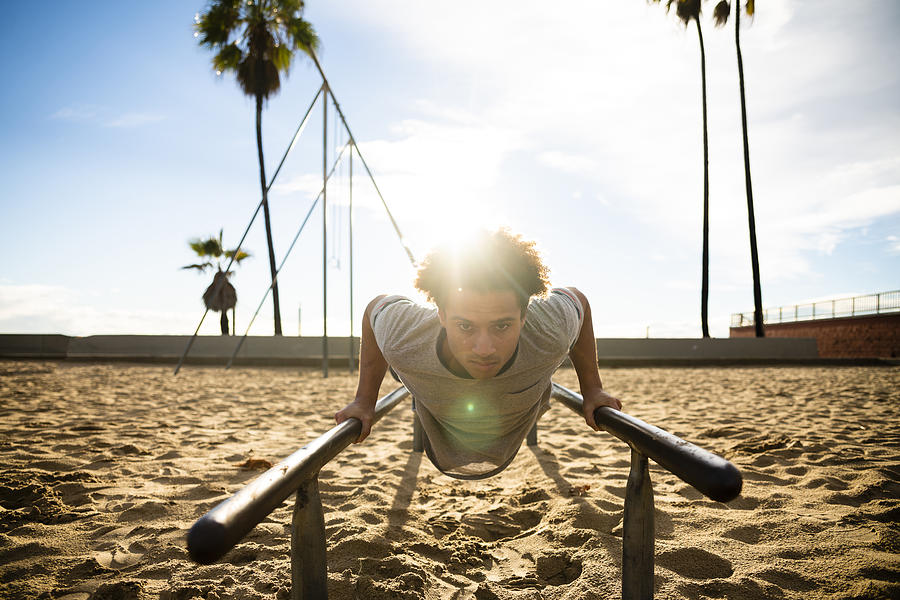 The young Latino man doing push-up exercise on the bars #1 Photograph by Alex Potemkin