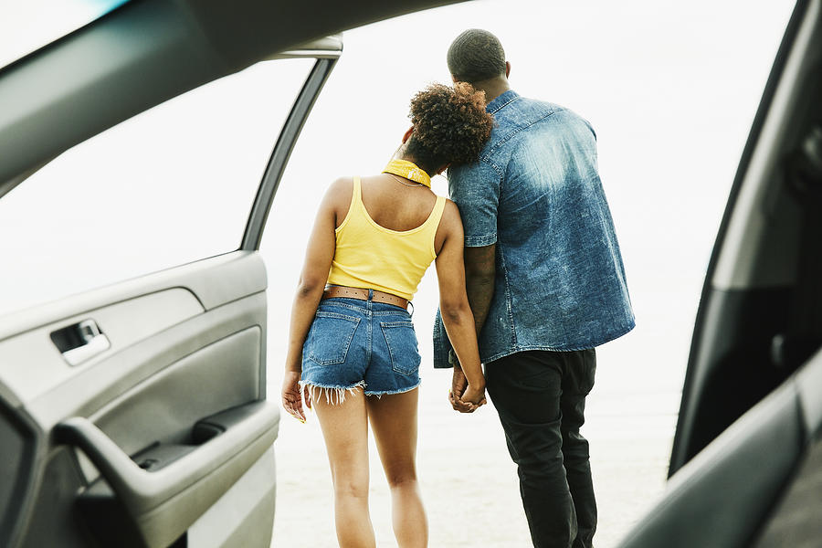 View through open car door of couple holding hands during trip to beach #1 Photograph by Thomas Barwick