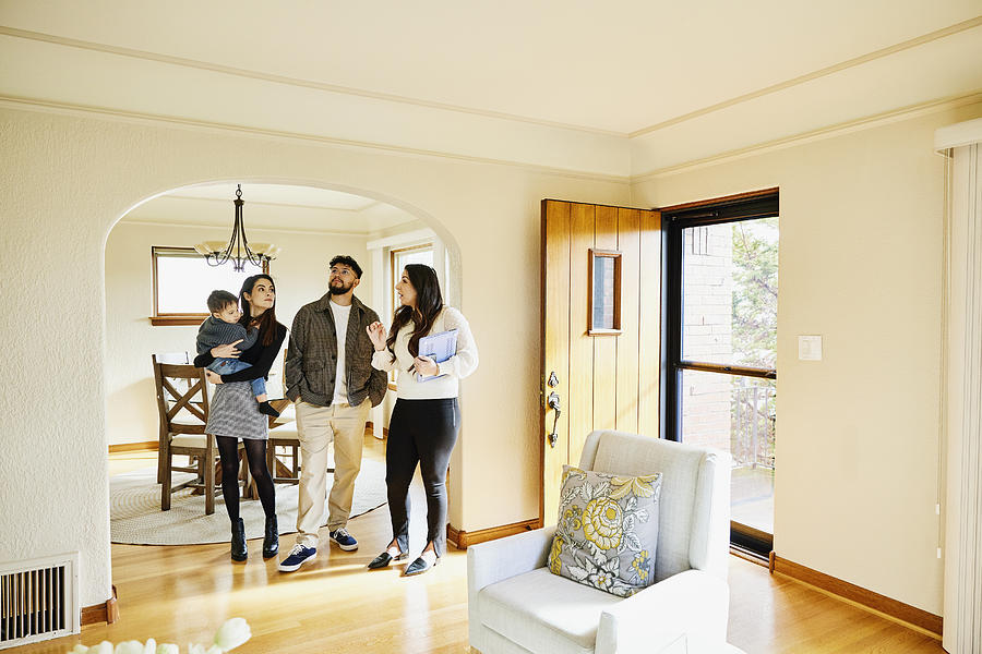Wide shot of family looking at home for sale with real estate agent #1 Photograph by Thomas Barwick