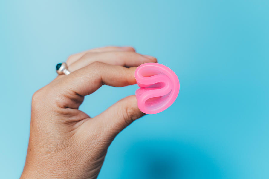Woman holding a pink menstrual cup on blue background #1 Photograph by Volanthevist