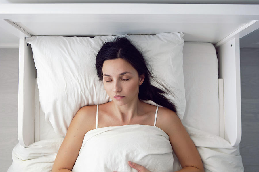 Woman In A White T-shirt Is Lying On The Bed And A Pillow Is Under The ...