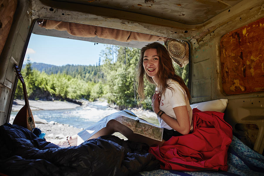 Woman resting in open camper, reading map. River in background Photograph by Janiecbros