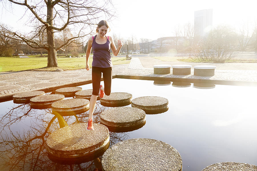 Woman running in city park across stepping stones #1 Photograph by Chris Tobin