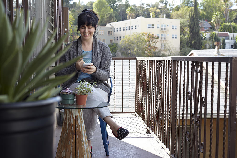 Woman using smartphone on balcony #1 Photograph by Rachael Porter