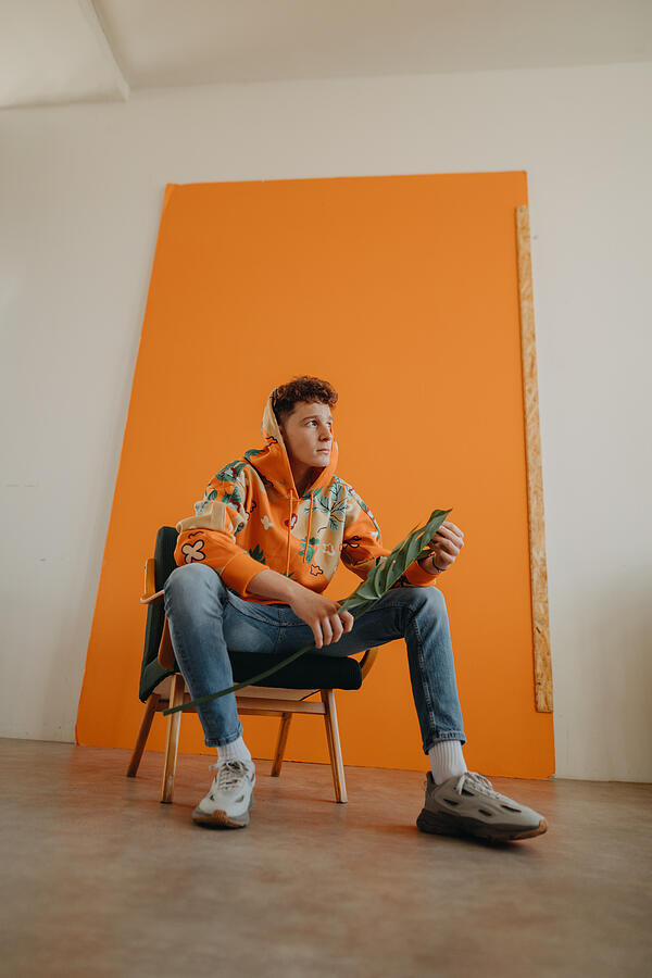 Young adult caucasian man sitting and posing in front of orange background. #1 Photograph by Halfpoint Images