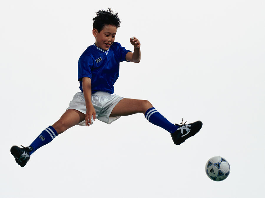 Young Asian boy kicking football in mid air #1 Photograph by Dex Image