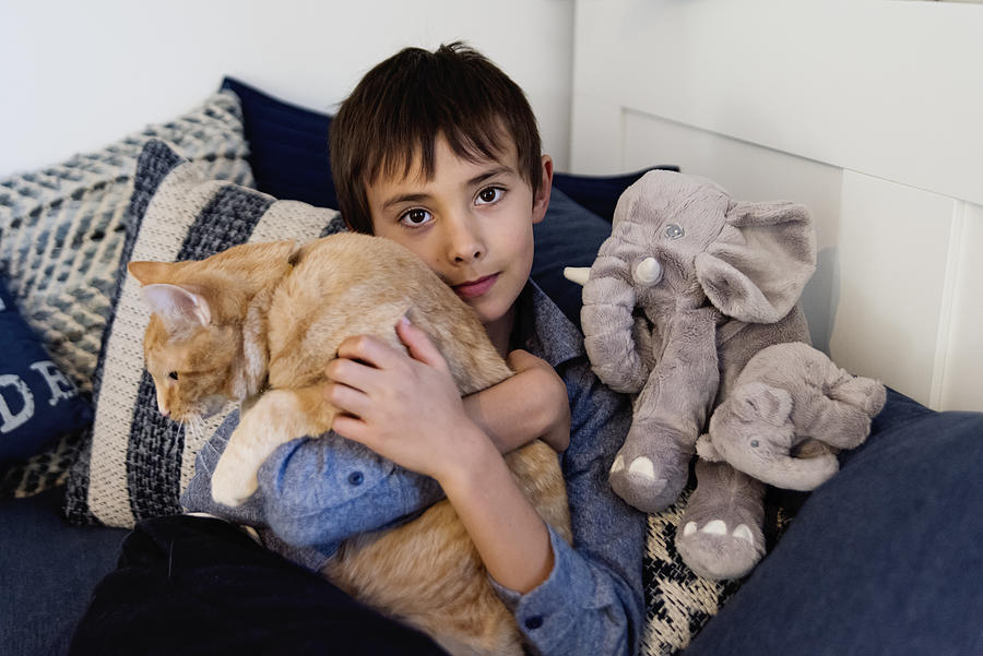 Young boy being comforted by holding his cat in bedroom. #1 Photograph by Martinedoucet