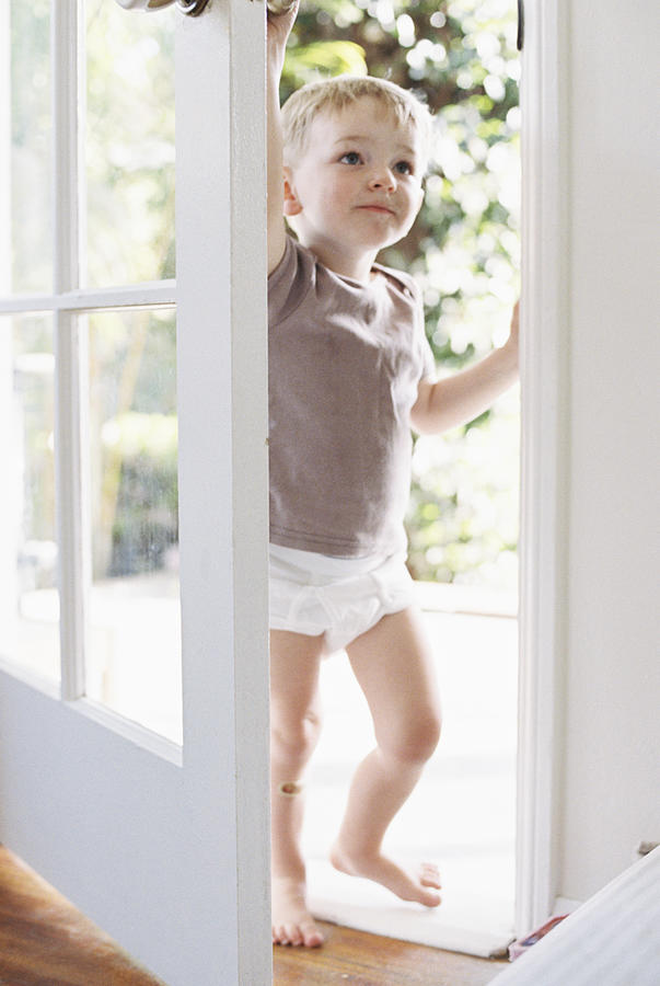 Young boy wearing T-Shirt and pants, opening a door. #1 Photograph by Mint Images
