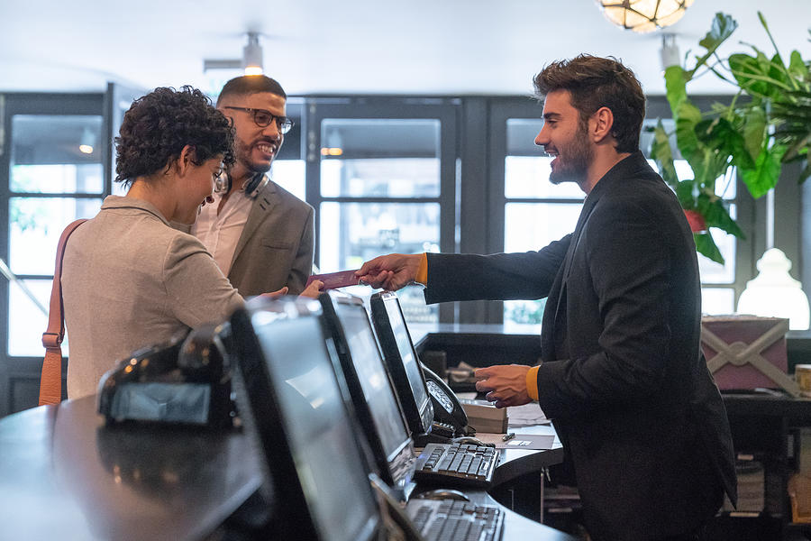 Young business couple checking in at hotel and receptionist man helping them. #1 Photograph by Authentic Images