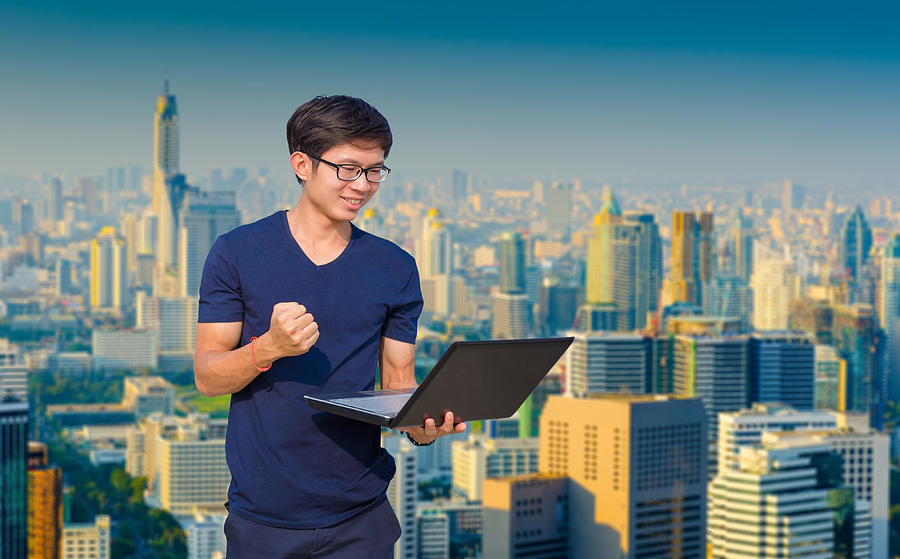 Young business man using laptop and digital tablet cityscape background #1 Photograph by Primeimages