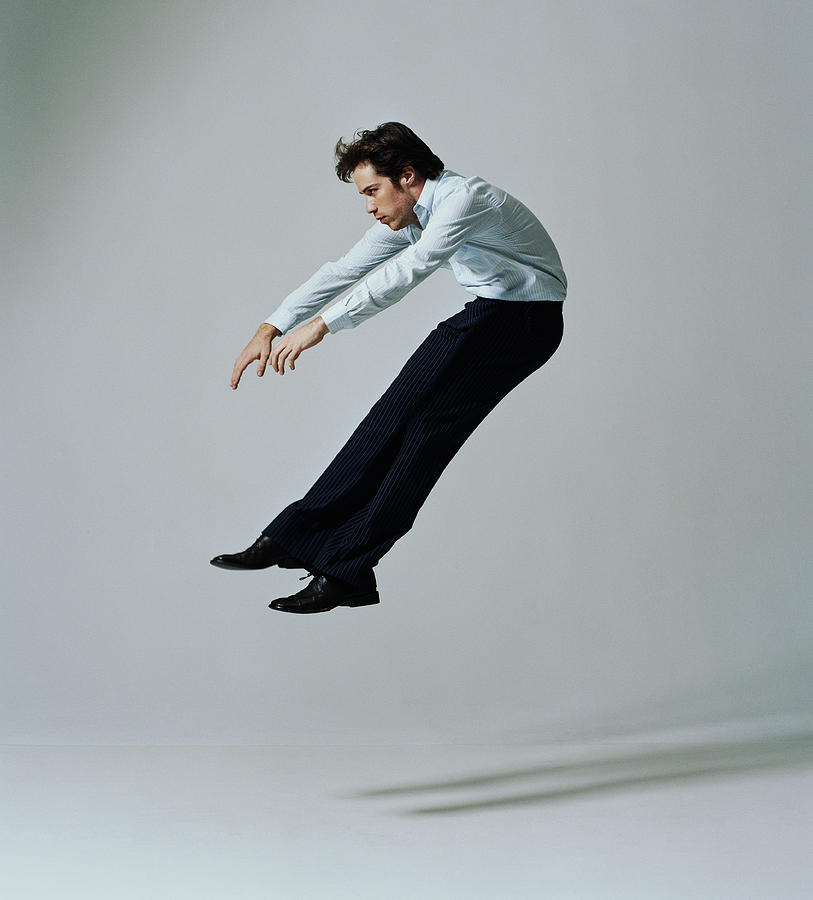 Young businessman flying backwards, side view #1 Photograph by PM Images