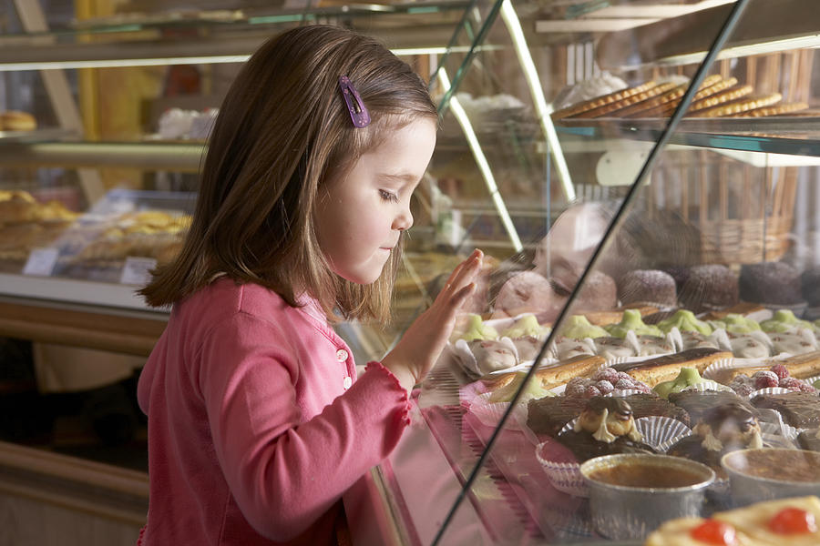 Young girl (9-11) looking at cakes in display cabinets, side view #1 Photograph by Rayes