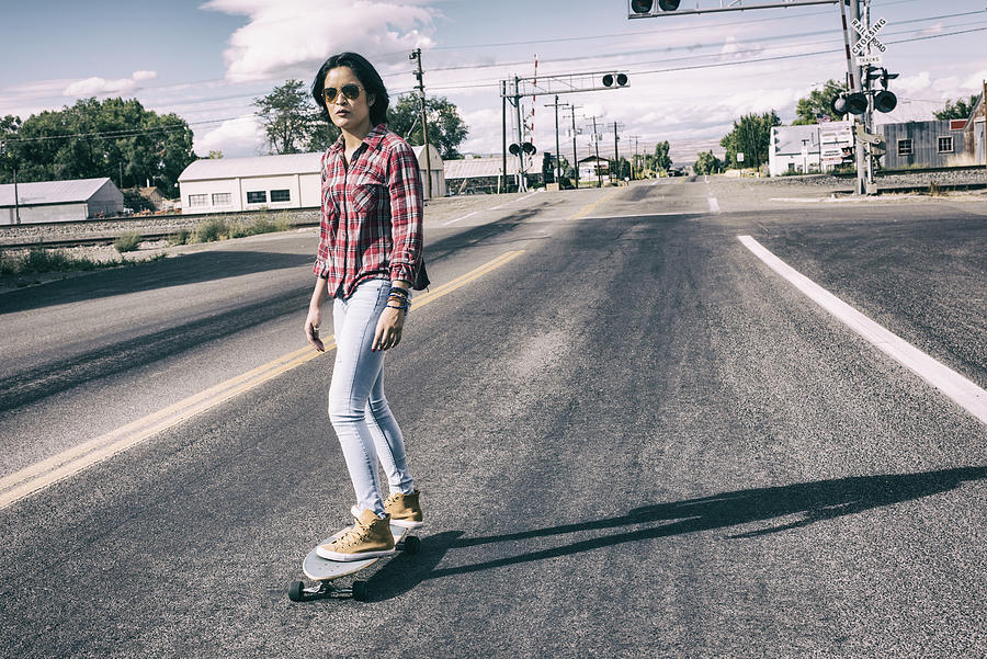 Young hispanic woman skateboarding on main street in a small town #1 Photograph by Tony Anderson