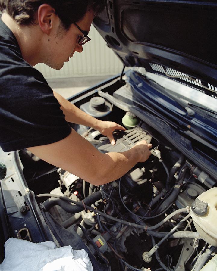 Young man checking a car battery #1 Photograph by Holger Hill
