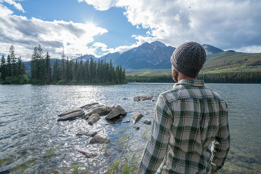 Young man standing by the lake looking at mountain scenery #1 Photograph by Swissmediavision