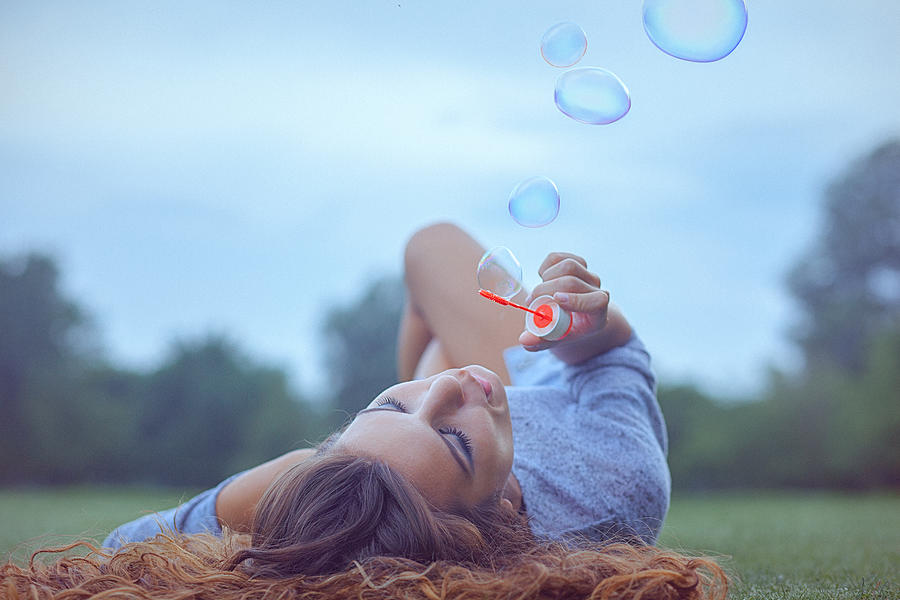 Young woman having fun and blowing bubbles outdoors #1 Photograph by Gruizza