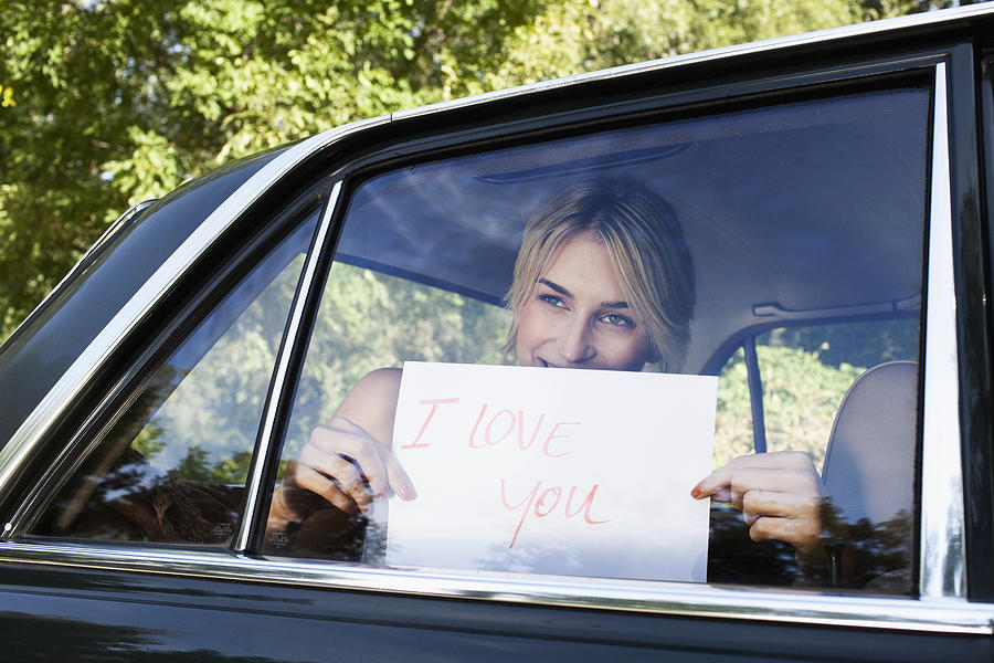 Young woman holding a sign saying I Love You up to a car window #1 Photograph by Oliver Rossi
