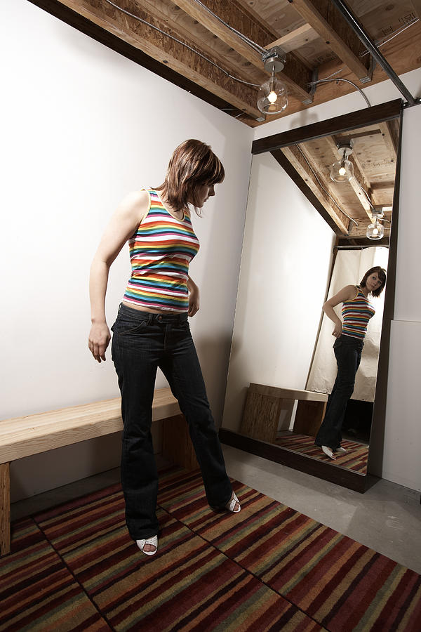 Young woman trying on clothing in dressing room, looking in mirror #1 Photograph by Thomas Northcut