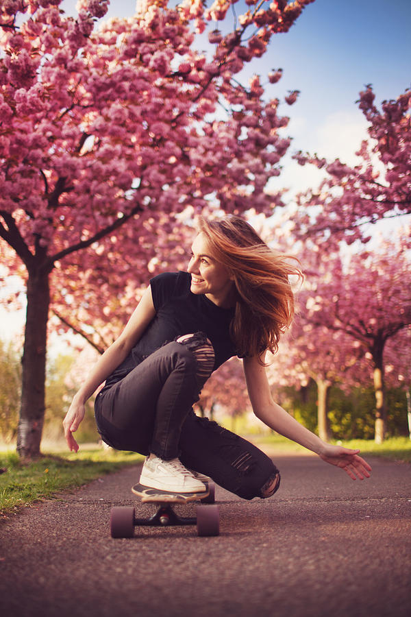 Young woman with longboard in cherry blossom alley #1 Photograph by Piskunov