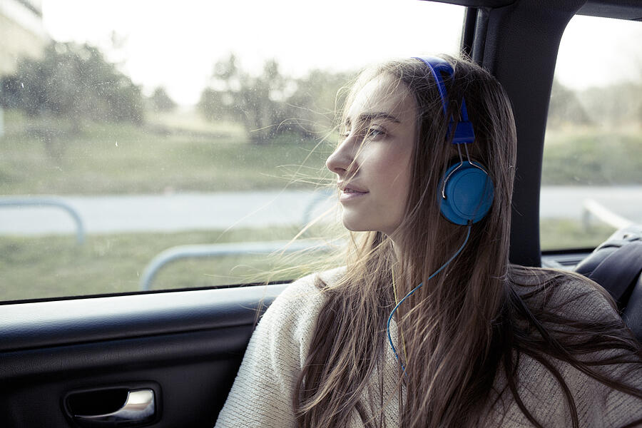 Young woman with windswept hair in a car wearing headphones #1 Photograph by Westend61