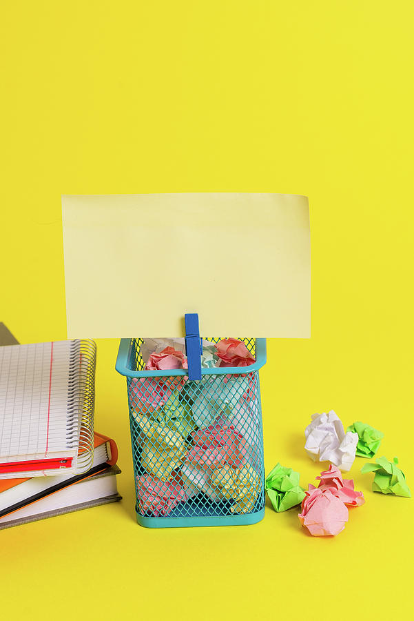 Ball Photograph - Little trash bin full of crumpled colored paper and a blue clothespin hanging a colorful note in a yellow background. Office supplies and empty reminder fixed on a can. #14 by Artur Szczybylo